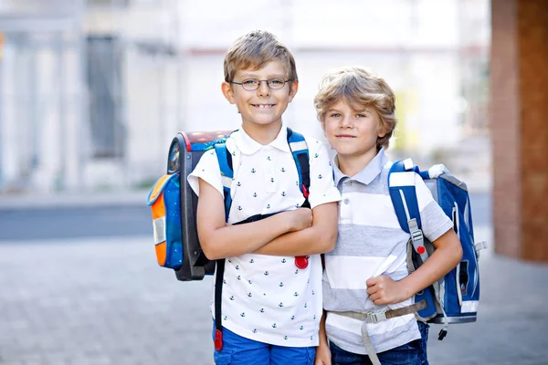 Két kisfiú hátizsákkal vagy táskával. Iskolába menet iskolások. Egészséges, imádnivaló gyerekek, testvérek és legjobb barátok az utcán, akik elhagyják otthonukat. Vissza a suliba. Boldog testvérek.. — Stock Fotó