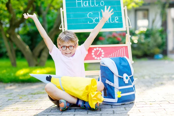 Happy little kid boy with glasses sitting by desk and backpack or satchel — Stock Photo, Image