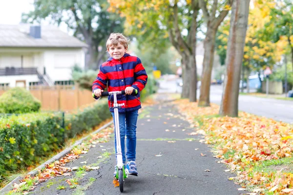 Bonito menino pré-escolar montando em scooter na cidade de outono — Fotografia de Stock