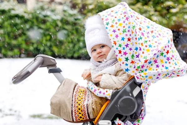 Schattig klein mooie babymeisje, zittend in de kinderwagen of wandelwagen op koude dag met regen, ijzel en sneeuw. — Stockfoto