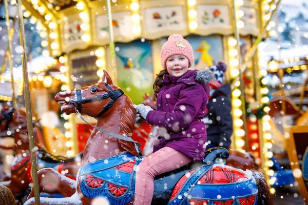 Adorable little kid girl riding on a carousel horse at Christmas funfair or market, outdoors. — Stock Photo, Image