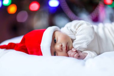 Noel Baba şapkası arka plan üzerinde renkli garland ışıkları ile Noel ağacı yakınındaki sağlıklı yeni doğan bebek. Portre sevimli çocuk, küçük kız veya erkek. Sevimli Noel wonde