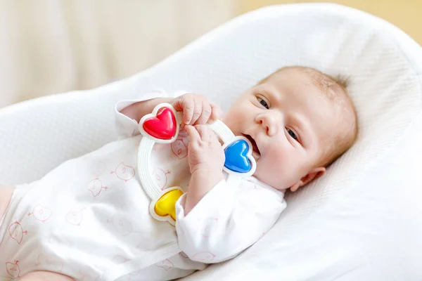 Cute healthy newborn baby playing with colorful rattle toy. in white bed at home. New born child, little girl looking surprised at the camera. Family, new life, childhood, beginning concept. — Stock Photo, Image