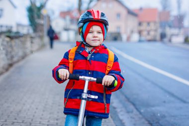 Sağlıklı küçük okul öncesi çocuk çocuk için okul veya okul öncesi sürme scooter sürme. Çocuk Aktiviteleri kış, ilkbahar veya sonbaharda açık. renkli moda giysileri ve kask ile komik mutlu çocuk