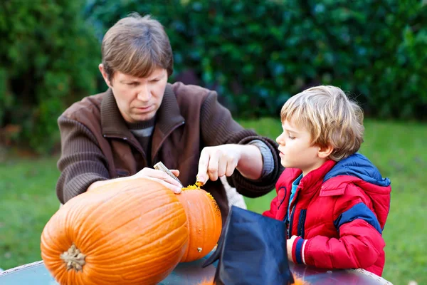 El joven papá y su pequeño niño haciendo jack-o-linterna para la calabaza de Halloween en el jardín de otoño, al aire libre. Padre e hijo, Familia divirtiéndose juntos . — Foto de Stock