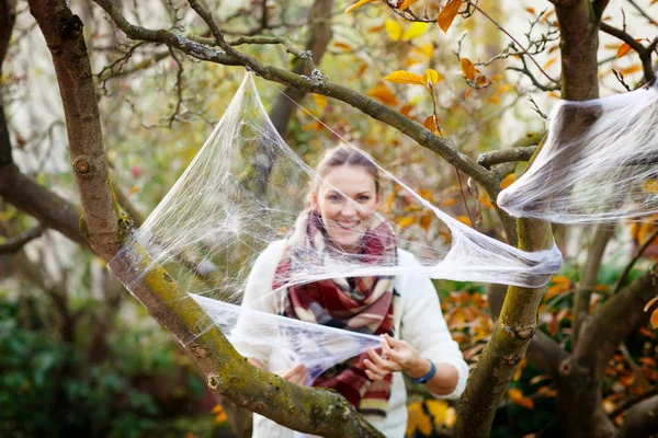 Jonge vrouw huis tuin versieren voor halloween met spinnenweb. Familie vieren vakantie. Selectieve aandacht op web — Stockfoto