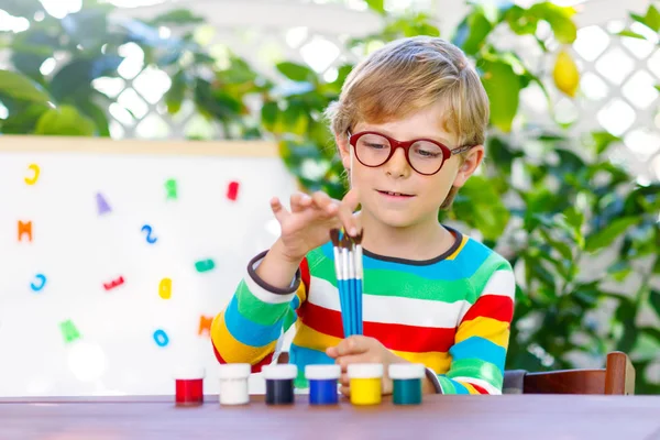 Grappige schattig kind jongetje met glazen holding aquarellen en borstels. Gelukkig kind en student is terug naar school. Onderwijs, school, leren concept. School, voorschoolse kwekerij apparatuur. — Stockfoto