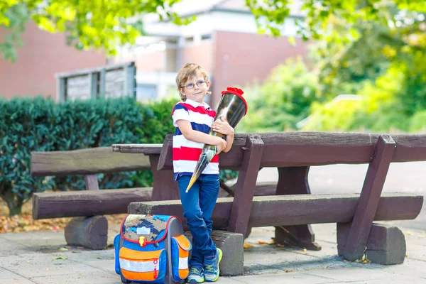 学校への彼の最初の日に眼鏡やバックパックやサッチェルを持つ幸せな小さな男の子。子供の屋外で暖かい晴れた日には、学校のコンセプトに戻る。子供とともに伝統的な通学路-ドイツ語. — ストック写真