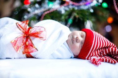 Bir haftalık güzel bir bebek, arka planda renkli çelenk ışıklarıyla Noel ağacının yanında battaniyeye sarılmış. Tatlı küçük çocuğun huzur içinde uyuduğu yakın plan. Aile, Xmas, doğum, yeni hayat: