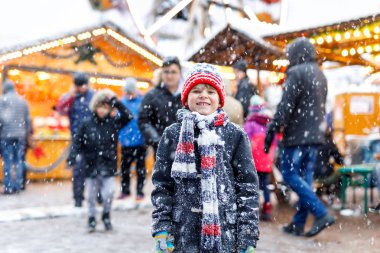 Küçük şirin çocuk şiddetli kar yağışında geleneksel Alman Noel pazarında eğleniyor. Mutlu çocuk Almanya, Münih 'te geleneksel aile pazarının tadını çıkarıyor. Renkli giysiler içinde gülen çocuk.