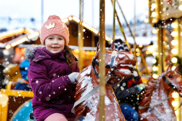 Adorable little kid girl riding on a merry go round carousel horse at Christmas funfair or market, outdoors. Happy child having fun on traditional family xmas market in Munich, Germany — Stock Photo, Image