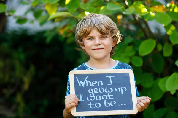 Glücklicher kleiner Junge mit Kreidetisch in der Hand. gesundes liebenswertes Kind im Freien auf dem Schreibtisch, wenn ich groß bin Ich möchte in Deutsch mit Traumberuf sein — Stockfoto