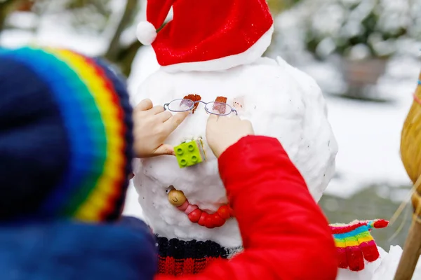 小孩把眼镜戴在雪人身上。特写。孩子们在冬天的第一场雪中玩乐 — 图库照片