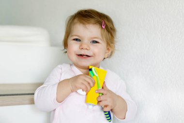 Küçük kız diş fırçası tutuyor ve ilk dişlerini fırçalıyor. Bebek süt dişini temizlemeyi öğreniyor. Önleme, hijyen ve sağlık hizmetleri kavramı. Banyoda mutlu bir çocuk