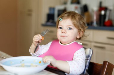 Kaşık püresi ve sebze püresinden yiyen sevimli bir kız bebek. Yemek, çocuk, beslenme ve gelişim konsepti - tatlı bebek, kaşıklı kız sandalyede oturuyor ve kendi kendine yemek yemeyi öğreniyor..