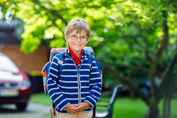 Ευτυχισμένο αγοράκι με γυαλιά και σακίδιο ή τσάντα την πρώτη του μέρα στο σχολείο ή στο νηπιαγωγείο. Παιδί σε εξωτερικούς χώρους σε ζεστή ηλιόλουστη μέρα, Επιστροφή στο σχολείο έννοια. — Φωτογραφία Αρχείου