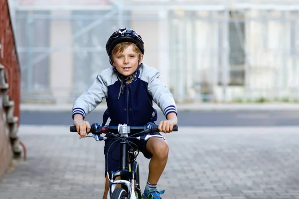 Skolpojke i skyddshjälm ridning med cykel i staden med ryggsäck. Glada barn i färgglada kläder cykling på cykel på väg till skolan. Säkert sätt för barn utomhus till skolan — Stockfoto