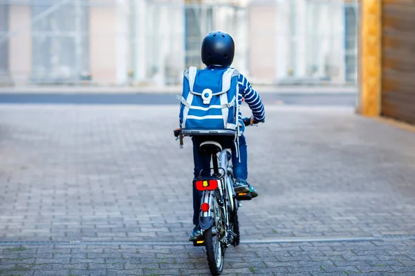 Школьник в защитном шлеме катается на велосипеде по городу с рюкзаком. Счастливый ребенок в красочной одежде катается на велосипеде по дороге в школу. Безопасный способ для детей на открытом воздухе в школу — стоковое фото