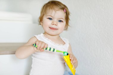 Küçük kız diş fırçası tutuyor ve ilk dişlerini fırçalıyor. Bebek süt dişini temizlemeyi öğreniyor..