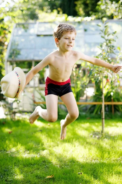 Söta aktiv unge pojke hoppar i trädgården på varma soliga sommardag. Lycklig unge tittar på kameran. Bedårande barn med blont hår och blå ögon — Stockfoto