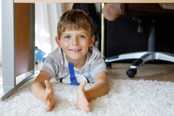 Belo Retrato de Menino Sorridente debaixo da mesa da escola. Um miúdo feliz a olhar para a câmara. Criança adorável com cabelos loiros e olhos azuis — Fotografia de Stock