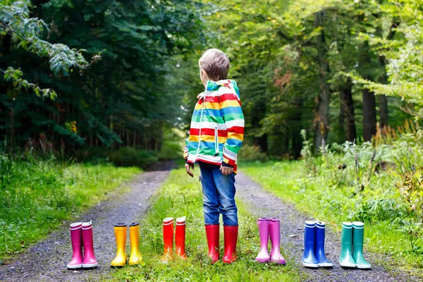 Little kid boy and group of colorful rain boots. Blond child standing in autumn forest. Close-up of schoolkid and different rubber boots. Footwear and fashion for rainy fall — Stock Photo, Image