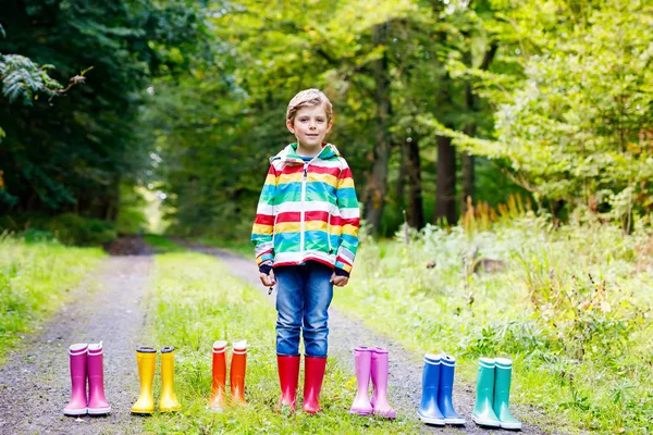 Menino e grupo de botas coloridas de chuva. Criança loira em pé na floresta de outono. Close-up de estudante e botas de borracha diferentes. Calçado e moda para queda chuvosa — Fotografia de Stock