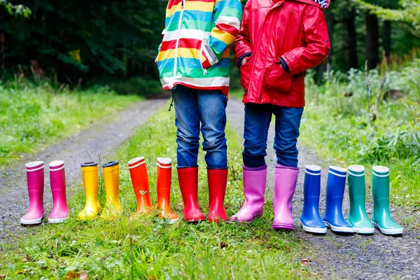 Niños pequeños, niños y niñas con botas de lluvia de colores. Niños de pie en el bosque de otoño. Primer plano de los escolares y diferentes botas de goma. Calzado y moda para el otoño lluvioso — Foto de Stock