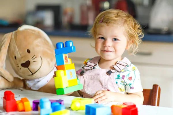 Menina da criança adorável com coelho de pelúcia favorito brincando com brinquedos educativos no berçário. Criança saudável feliz se divertindo com blocos de plástico diferentes coloridos em casa. Bonito bebê aprendizagem criação. — Fotografia de Stock