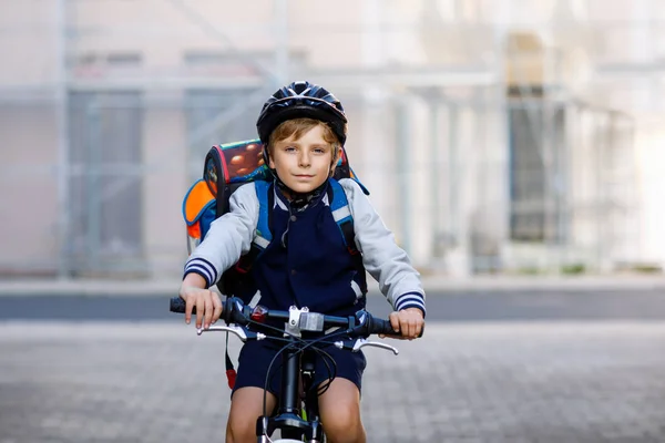 Schoolkid boy in safety helmet riding with bike in the city with backpack. Happy child in colorful clothes biking on bicycle on way to school. Safe way for kids outdoors to school — Stock Photo, Image