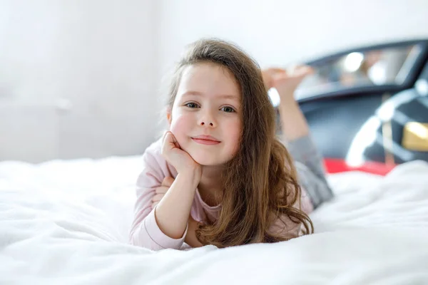 Entzückend glückliches kleines Mädchen, nachdem es in seinem weißen Bett in bunter Nachtwäsche geschlafen hat. — Stockfoto