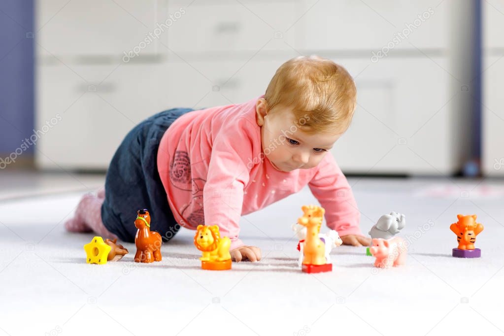 Adorable baby girl playing with domestic toy pets like cow, horse, sheep, dog and wild animals like giraffe, elephant and monkey. Happy healthy child having fun with colorful different toys at home