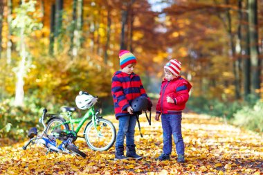 İki küçük çocuklar kask koyarak sonbahar ormandaki bisiklet ile çocuk