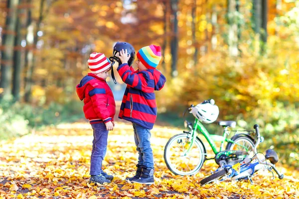 Két kis gyerek kerékpár sisakok elhelyezés őszi erdőben fiúk — Stock Fotó