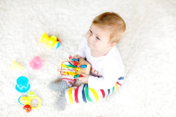 Adorável menina brincando com brinquedos educativos no berçário. Criança saudável feliz se divertindo com brinquedos diferentes coloridos em casa. Desenvolvimento do bebê e primeiros passos, aprendendo a jogar e agarrar. — Fotografia de Stock