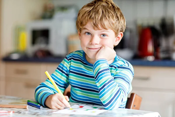 Muotokuva söpö terve onnellinen koulupoika kotona tehdä kotitehtäviä. Pieni lapsi kirjallisesti värikkäitä kyniä, sisätiloissa. Ala-aste ja koulutus. Lapsi oppii kirjoittamaan kirjeitä ja numeroita — kuvapankkivalokuva