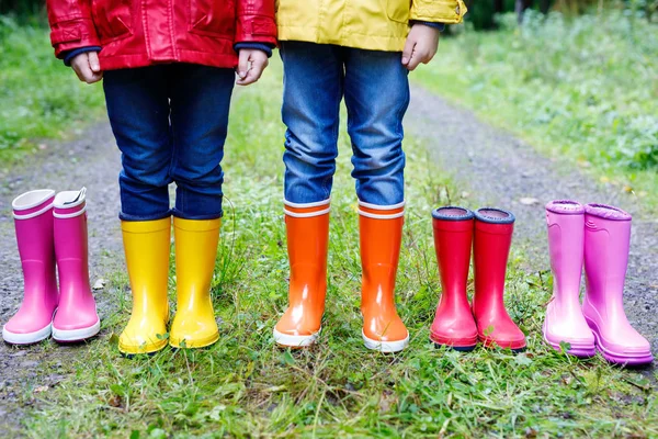 Niños pequeños, niños y niñas con botas de lluvia de colores. Niños de pie en el bosque de otoño. Primer plano de los escolares y diferentes botas de goma. Calzado y moda para el otoño lluvioso — Foto de Stock
