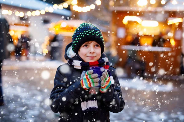 Little cute kid boy drinking hot children punch or chocolate on German Christmas market. Happy child on traditional family market in Germany, Laughing boy in colorful winter clothes — Stock Photo, Image