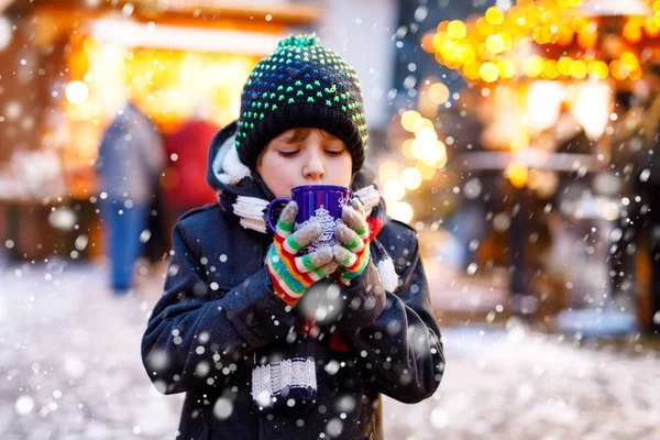 Little cute kid boy drinking hot children punch or chocolate on German Christmas market. Happy child on traditional family market in Germany, Laughing boy in colorful winter clothes — Stock Photo, Image