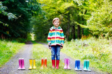 Küçük çocuk çocuk ve renkli yağmur botları grup. Sarışın çocuk sonbahar ormanda ayakta. Temel ve farklı lastik çizme Close-up. Ayakkabı ve moda yağmurlu sonbahar için