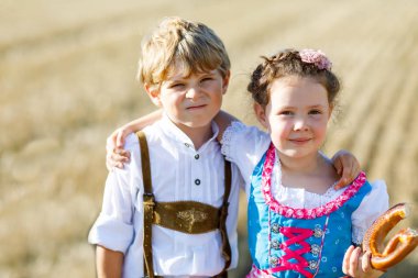 Buğday tarlasında geleneksel Bavyera kostümlü iki çocuk. Alman çocukları Ekim Festivali sırasında ekmek ve simit yiyorlar. Almanya 'da yaz aylarında erkek ve kız saman balyalarında oynuyorlar..
