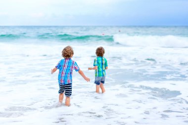 Okyanus sahilinde koşan iki mutlu çocuk. Komik şirin çocuklar, kardeşler ve en iyi arkadaşlar tatildeler ve fırtınalı bir günde Miami, Florida, ABD 'de tatilin tadını çıkarıyorlar..