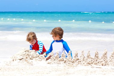İki küçük çocuk Meksika Playa del Carmen plajında kumdan kale inşa ederken eğleniyor. Çocuklar tatillerinde birlikte oynuyorlar. İkizler, mutlu kardeşler gülüyor ve gülüyorlar..