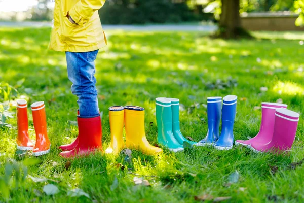 Little kid, boy or girl in jeans and yellow jacket in colorful rain boots. Close-up of child with different rubber boots. Footwear for rainy fall. Concept of bright autumn. — Stock Photo, Image