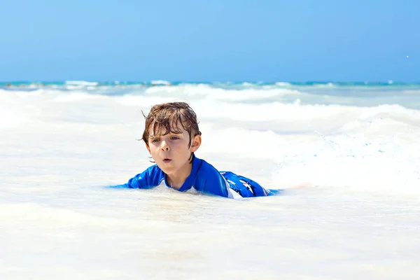 Adorable niño rubio divirtiéndose en la playa tropical de Maldivas. Emocionado niño jugando y surfeando en traje de baño protegido contra el sol en el océano en vacaciones — Foto de Stock