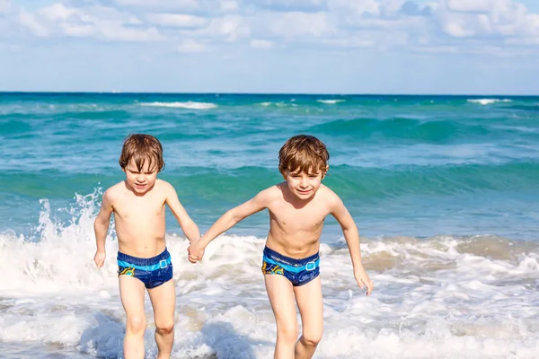 Dwa szczęśliwy mało dzieci chłopców uruchomiona na plaży oceanu. Zabawny ładny dzieci, rodzeństwo, bliźniaki i przyjaciele Dokonywanie wakacje i cieszyć się latem na burzliwy słoneczny letni dzień. Miami, Florida — Zdjęcie stockowe
