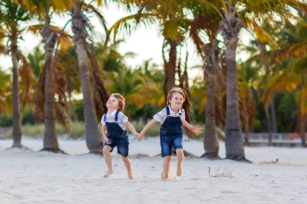 Due bambini piccoli ragazzi che si divertono sulla spiaggia tropicale, felici migliori amici che giocano, concetto di amicizia. Fratelli fratelli, i gemelli in famiglia guardano correndo con palme su sfondo. Vacanze in famiglia . — Foto Stock