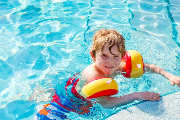 Ragazzino felice che si diverte in piscina. Bambino felice attivo imparare a nuotare. con galleggianti sicuri o nuotate. Famiglia, vacanze, concetto estivo — Foto Stock