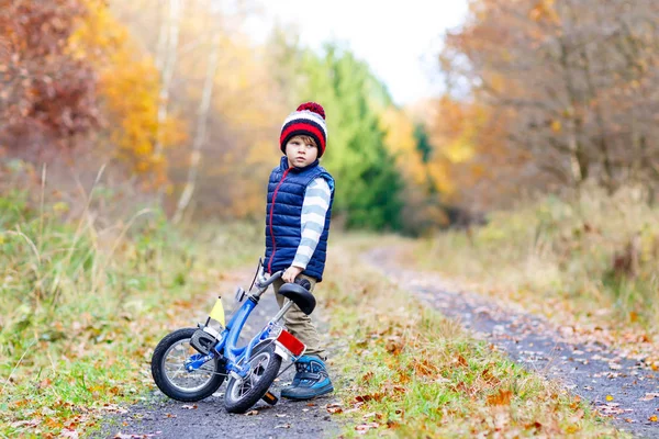 Menino em roupas quentes coloridas no outono parque florestal dirigindo bicicleta. Ciclismo infantil ativo no dia ensolarado de outono na natureza. Segurança, esportes, lazer com conceito de crianças. Moda casual para crianças. — Fotografia de Stock