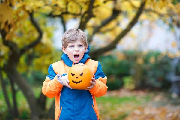 Happy cute little kid boy with halloween pumpkin lantern. Funny child in colorful clothes having fun and playing in autumn garden on cold autumnal day. Scary jack-o-lantern, celebration of holiday. — Stock Photo, Image